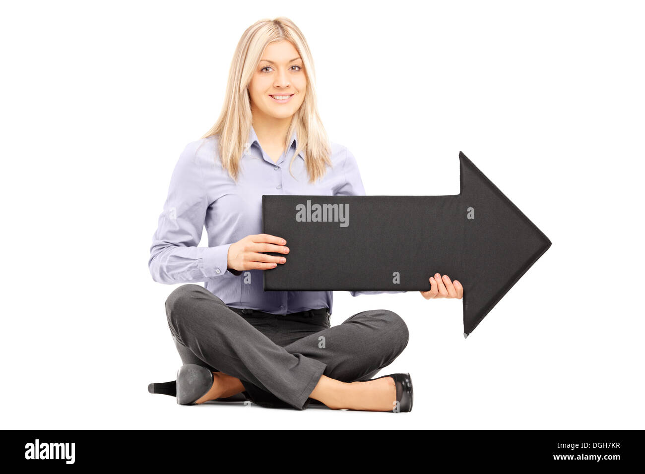 Young blond woman seated on floor holding a big black arrow pointing to ...
