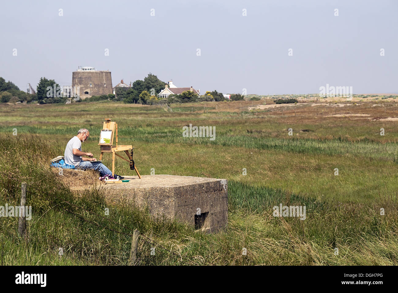 Artist sitting on World War 2 pill box looking over Oxley marsh at Shingle Street, Suffolk. Note the Martello Tower number AA. Stock Photo
