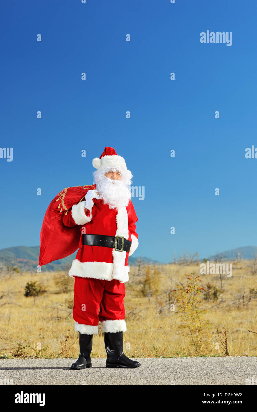 Full length portrait of a Santa claus with bag standing on an open road ...