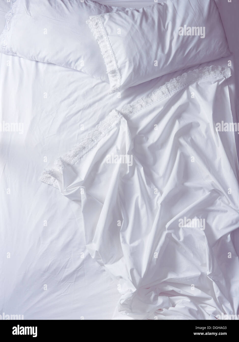 Empty unmade bed with ruffled white sheets in morning light, high angle view. Stock Photo