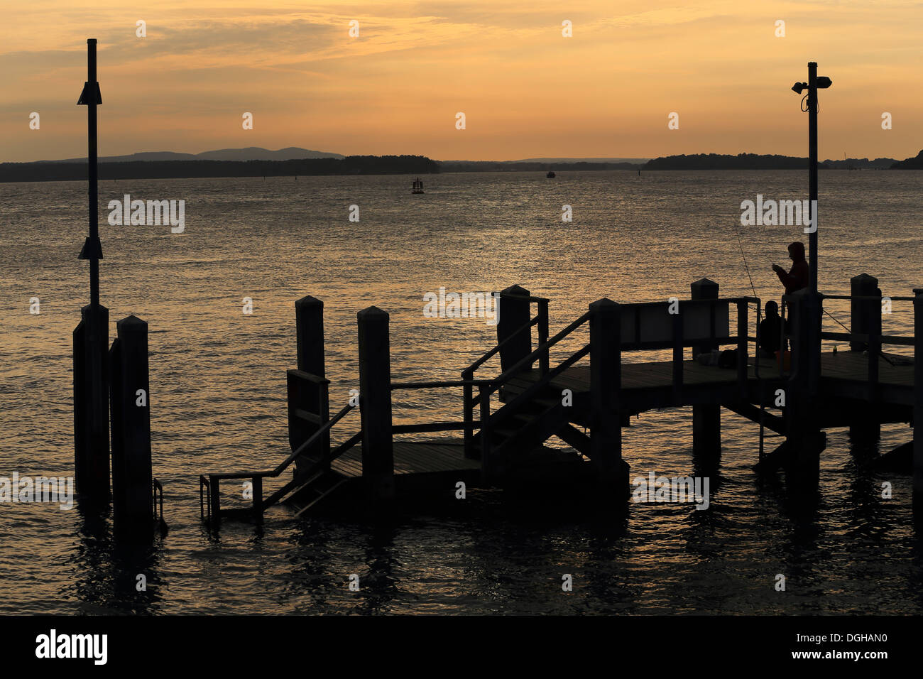Poole Harbour, Dorset. Sunset across the water to the Purbeck Hills with fisherman on boat jetty Stock Photo