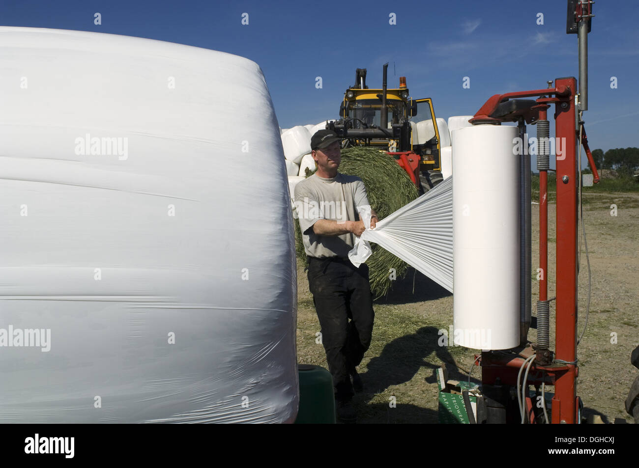 Farmer plastic wrapping round silage bales with mechanical balewrapper