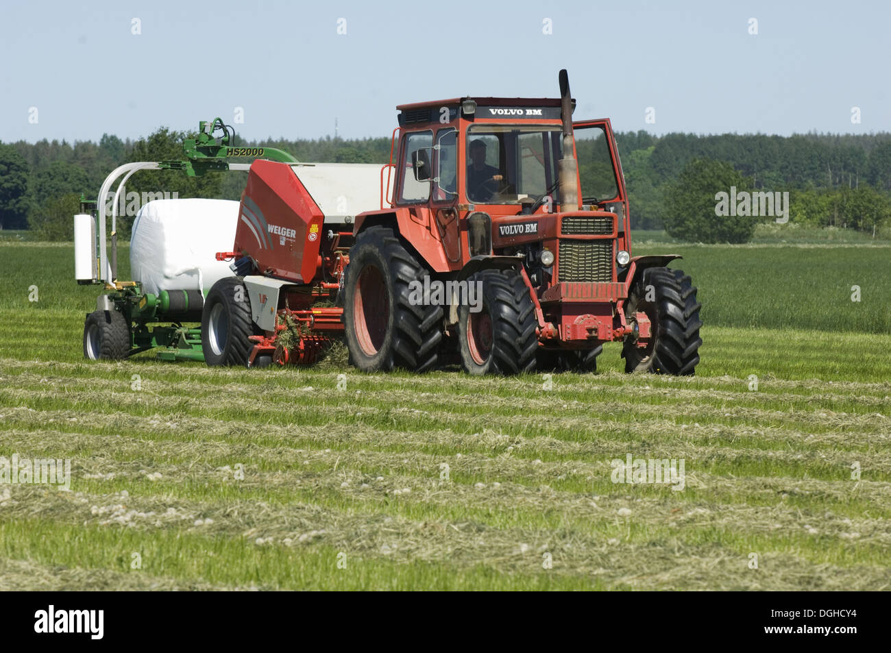 Volvo tractor pulling round baler and mechanical bale-wrapper, plastic wrapping round silage bale, Sweden Stock Photo