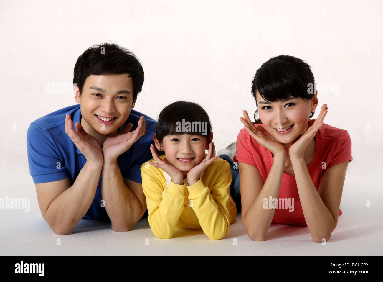 East Asian family with one child lying on the floor, holding faces, smiling, looking at camera Stock Photo