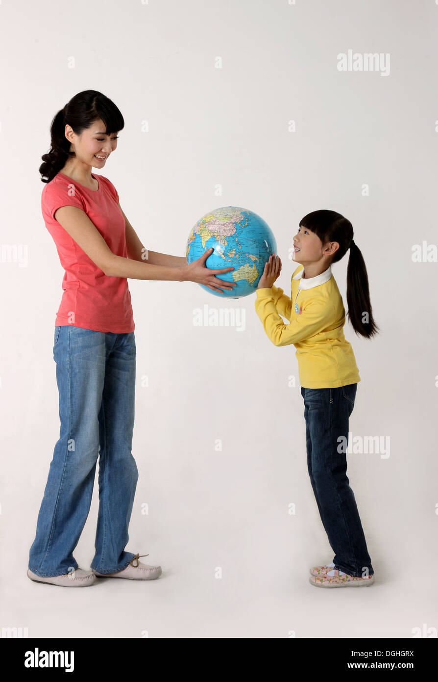 East Asian mother and daughter standing on the floor holding a globe, looking at each other Stock Photo