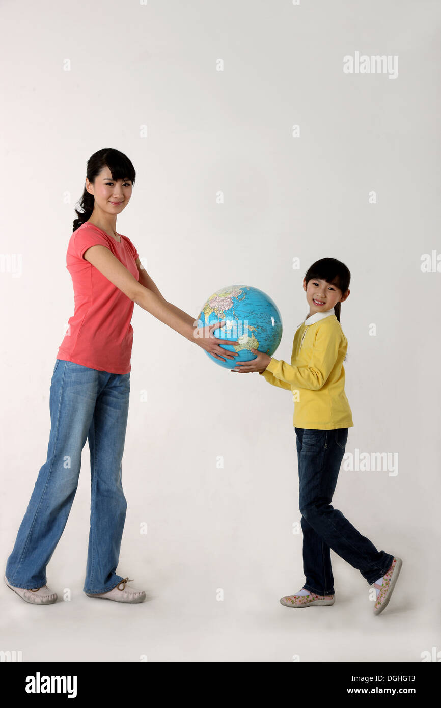 East Asian mother and daughter standing on the floor holding a globe, smiling, looking at the camera Stock Photo