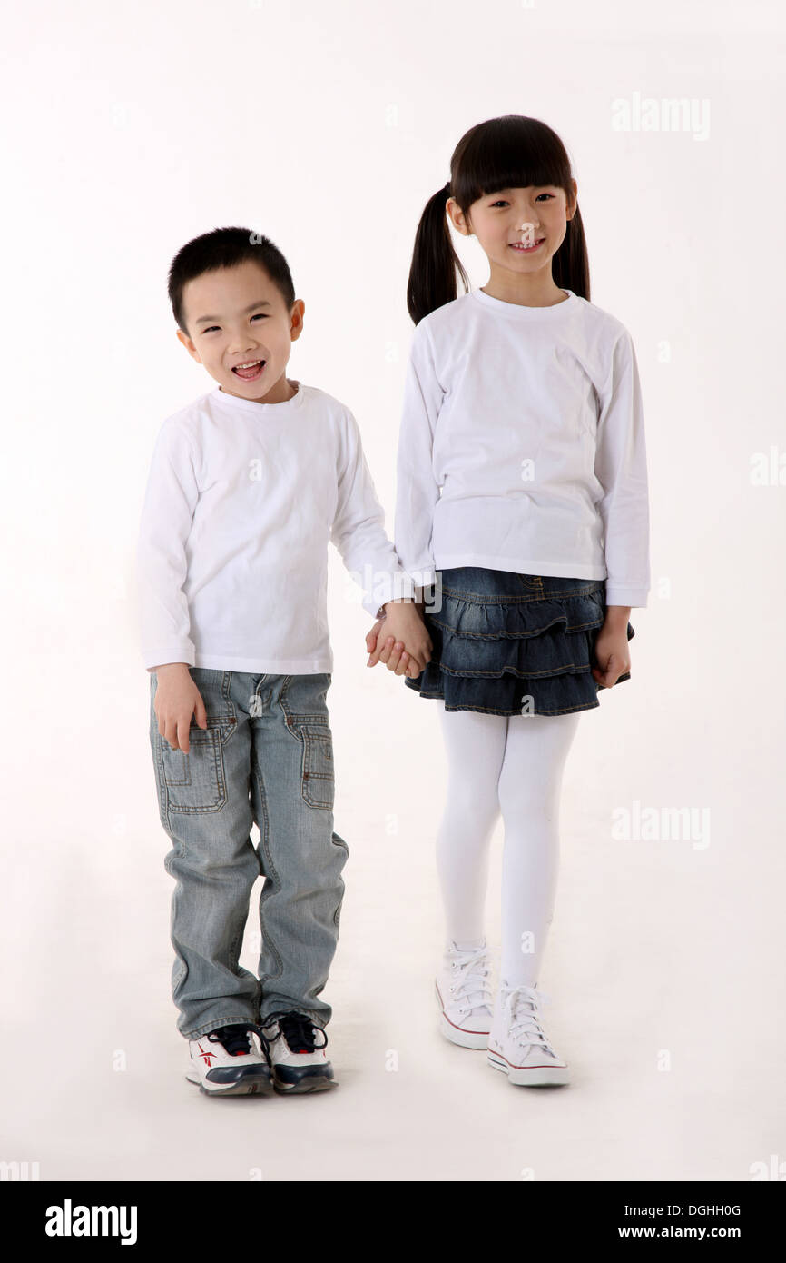 East Asian boy and girl standing on the floor, hand in hand, smiling, looking at the camera Stock Photo