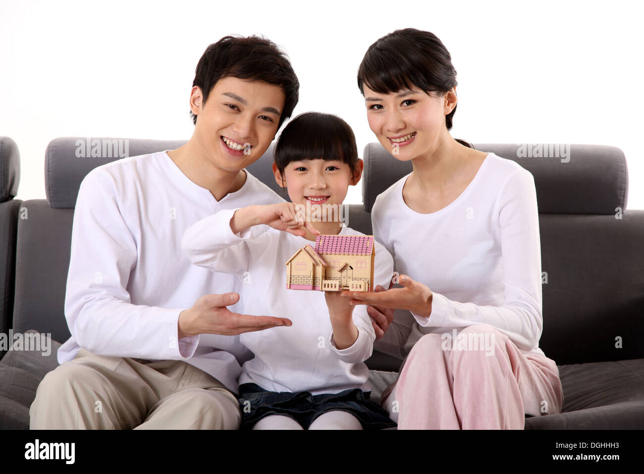 East Asian family with one child sitting on the sofa, holding a model house Stock Photo