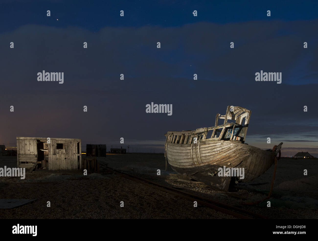 Abandoned fishing boat and fisherman hut on shingle beach at night ...