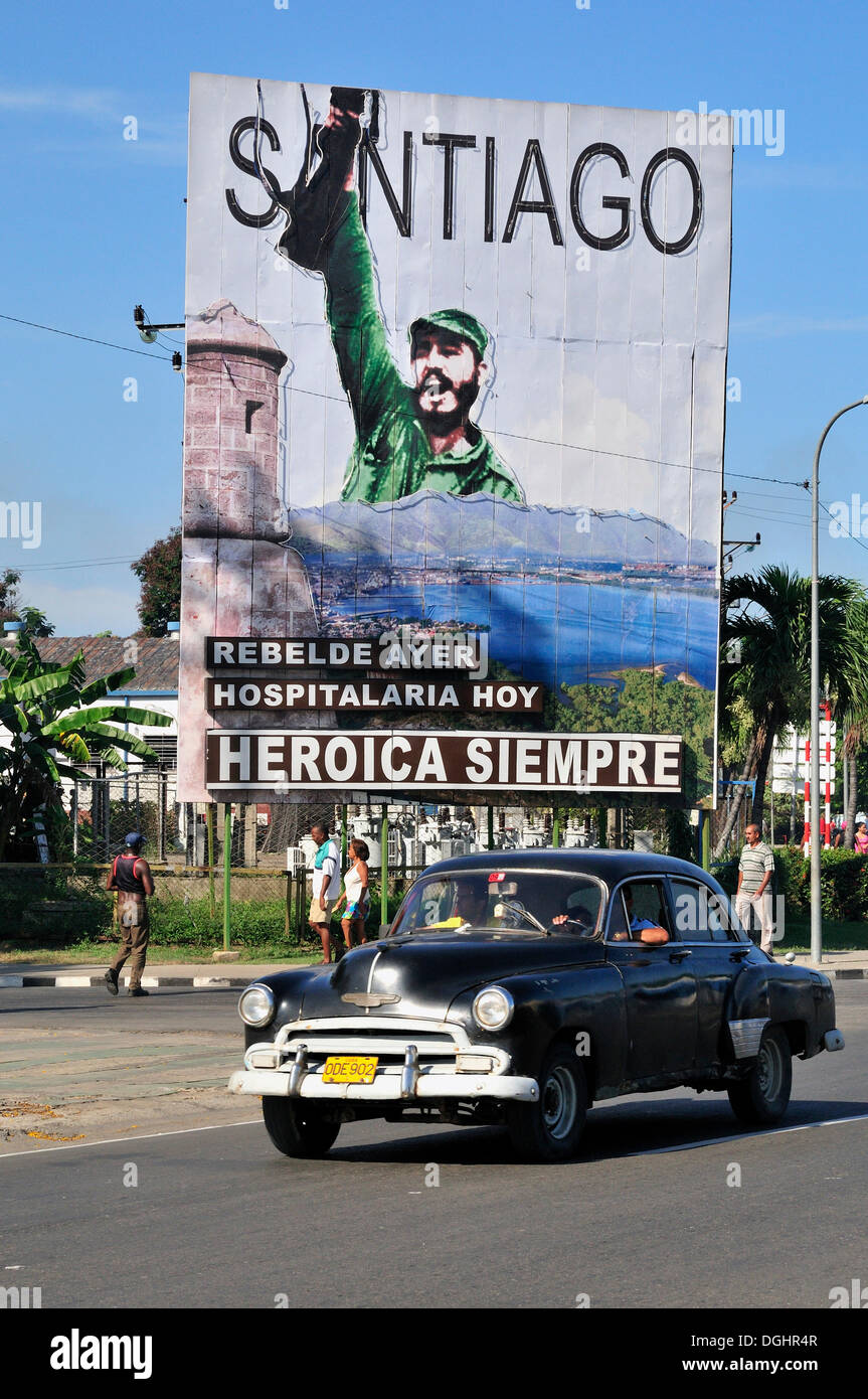 Vintage car driving in front of revolutionary propaganda poster, 'Santiago siempre heróica', Spanish for 'Santiago is always Stock Photo