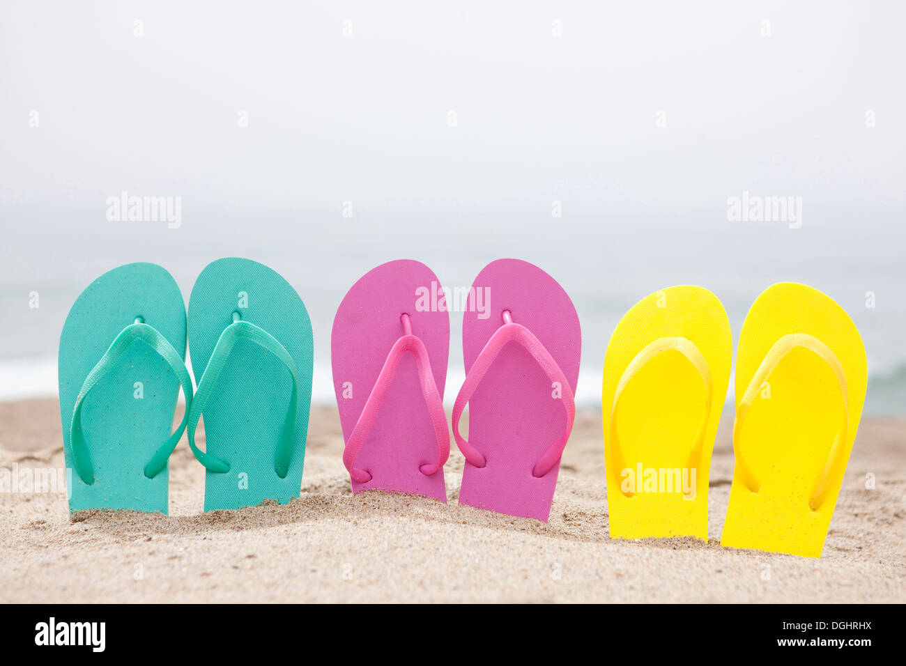 three pairs of flip flops on a beach Stock Photo - Alamy