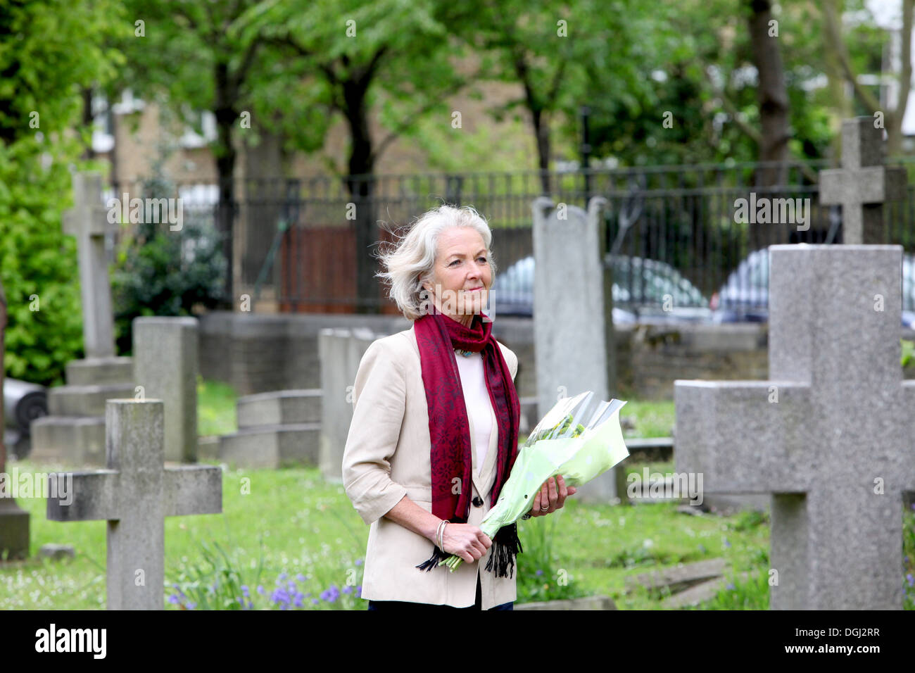 Senior woman holding flowers in graveyard Stock Photo
