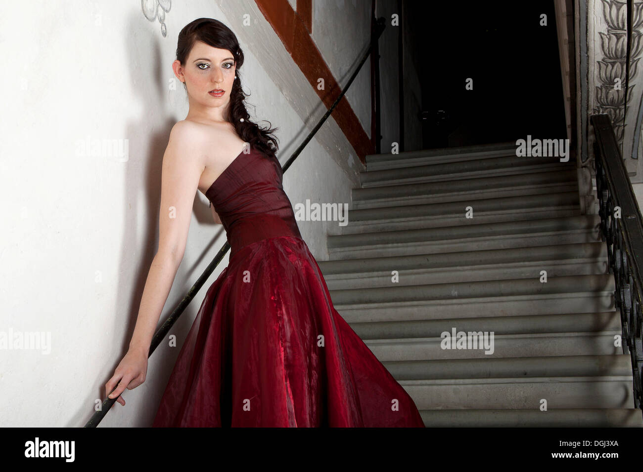 Young woman wearing a red dress standing on the stone stairs in a stairwell Stock Photo