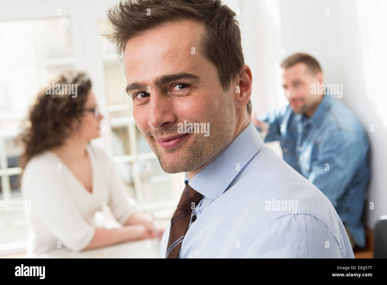 Mature man smiling at camera, mid adults in background Stock Photo