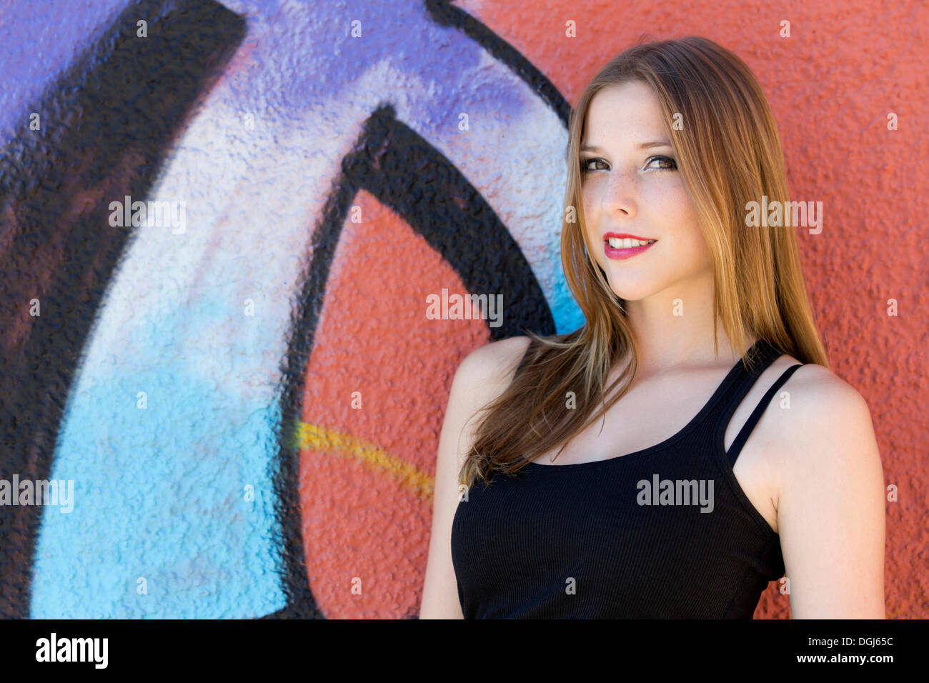 Young woman in a black top posing in front of a graffiti wall, portrait Stock Photo