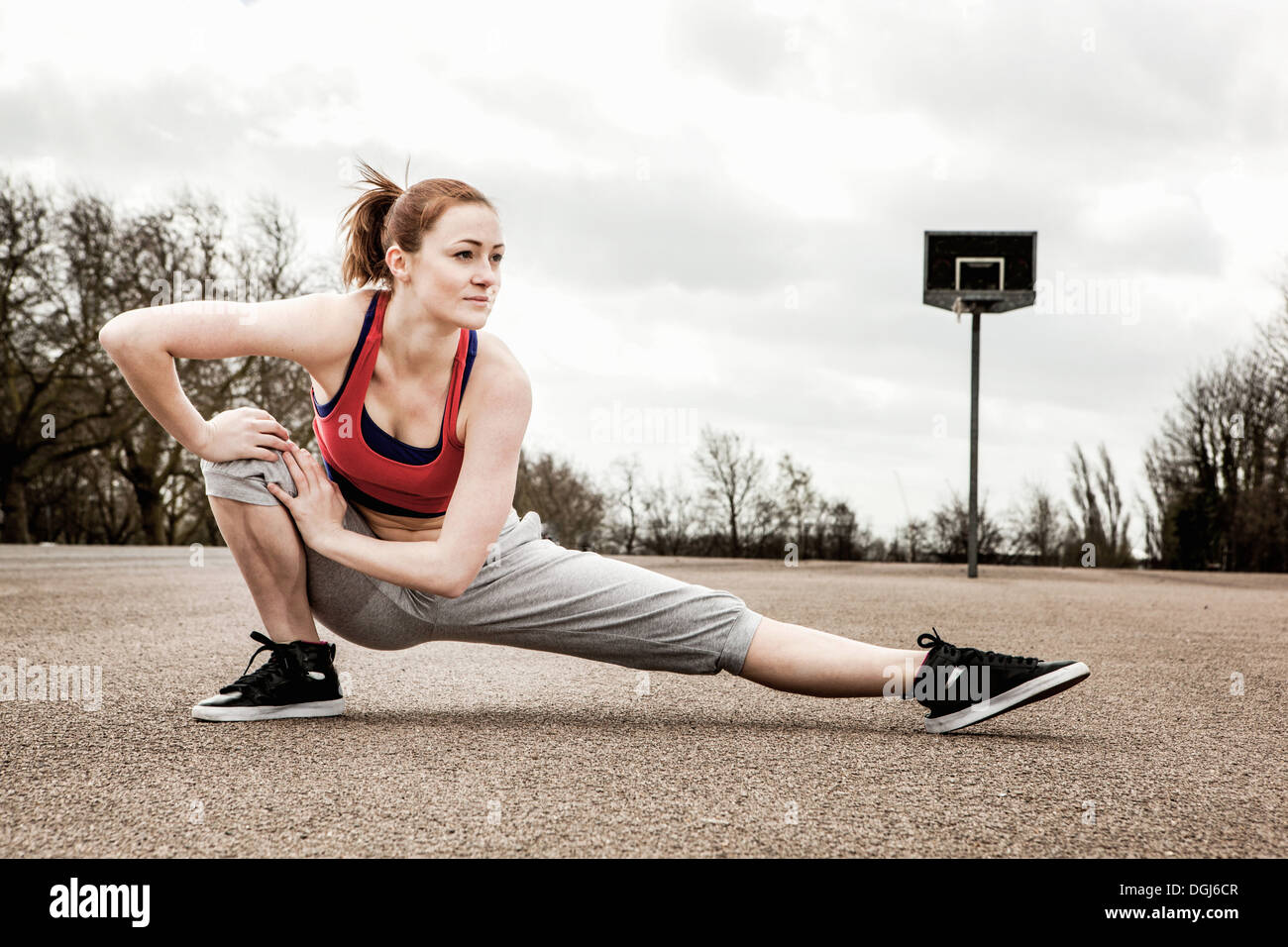 Woman stretching left leg and bending right leg on court Stock Photo
