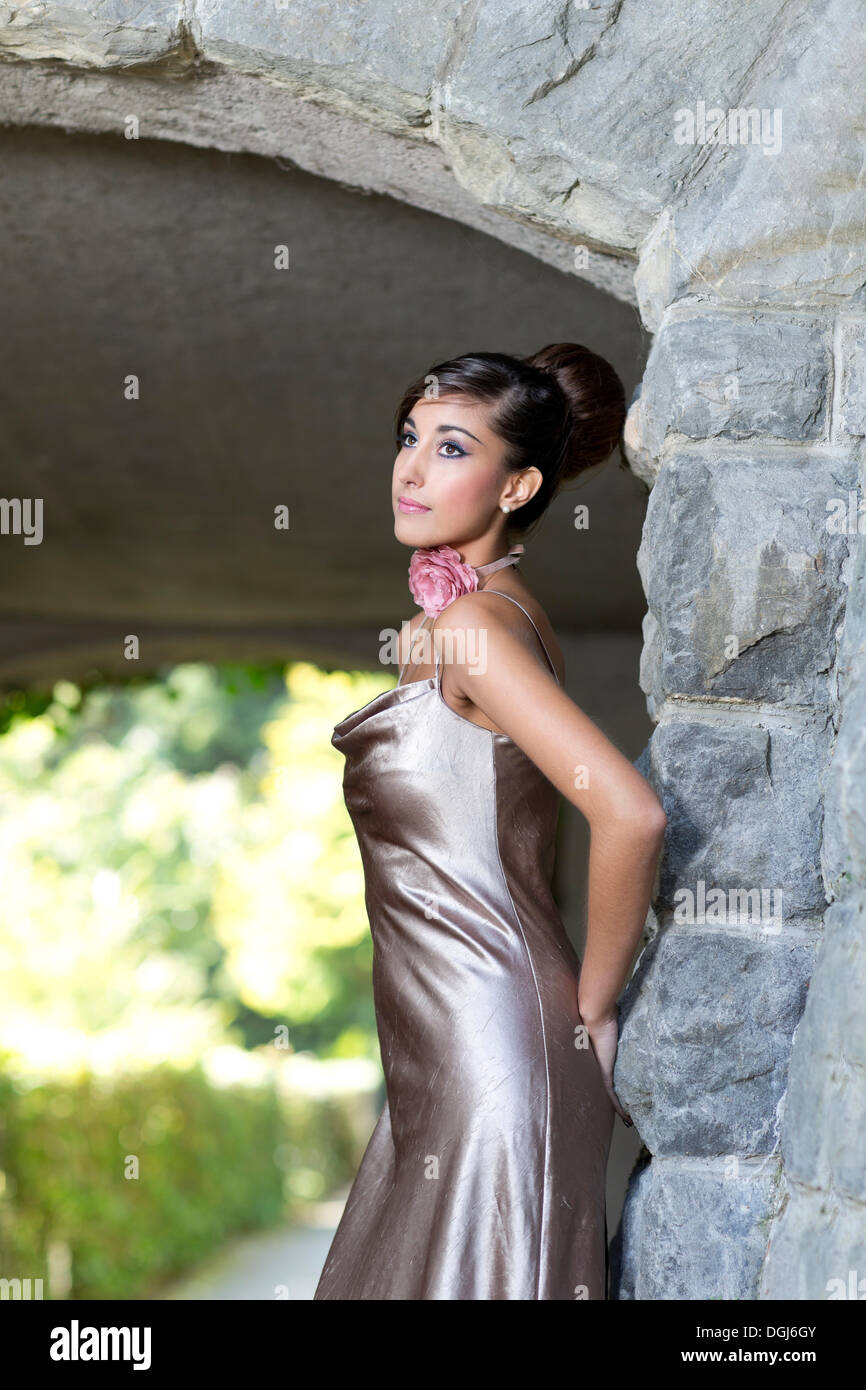 Young woman with an updo hairstyle and a silvery evening dress posing in front of an archway Stock Photo