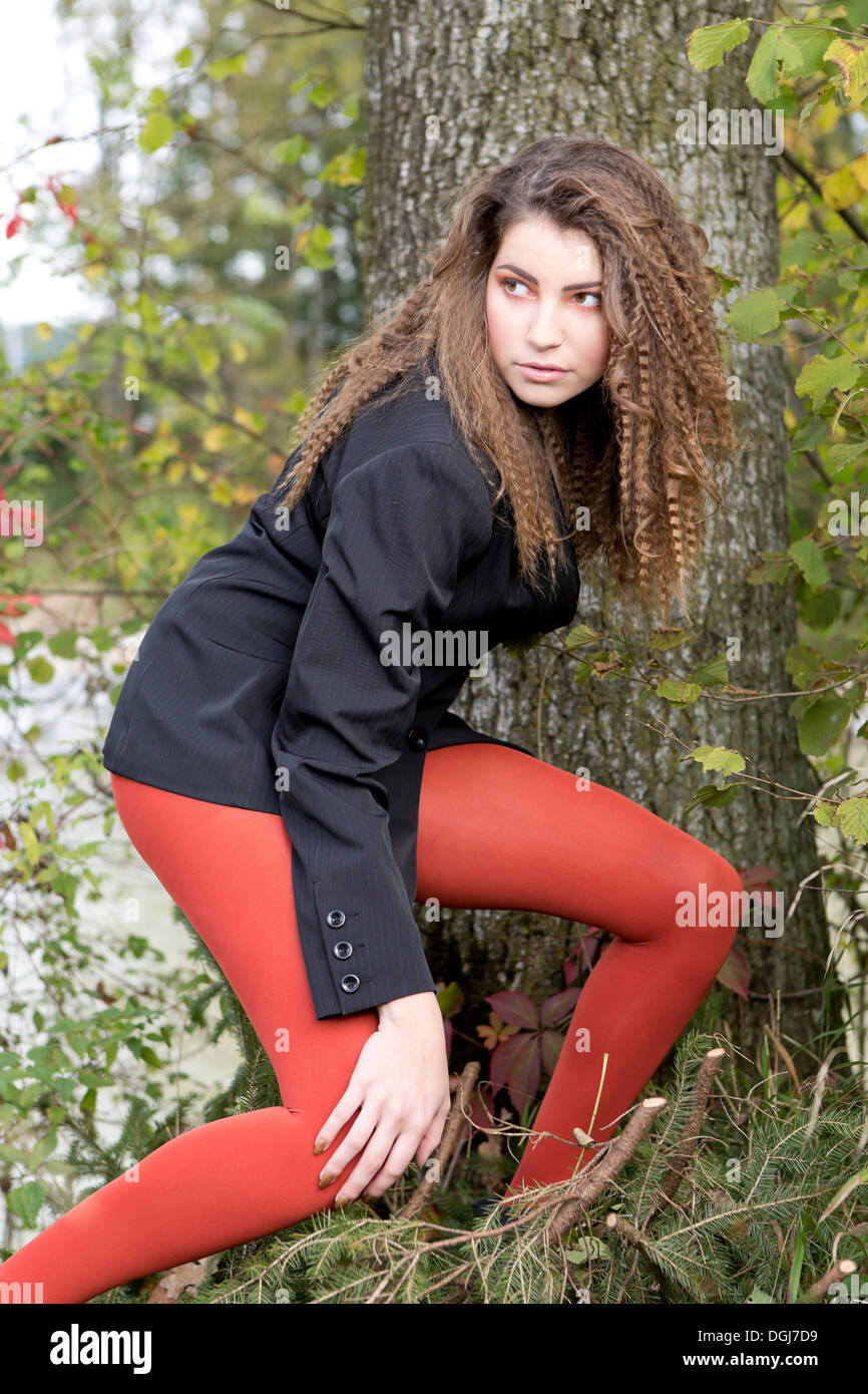 Young woman wearing a dark blazer and red pantyhose posing in front of a tree Stock Photo