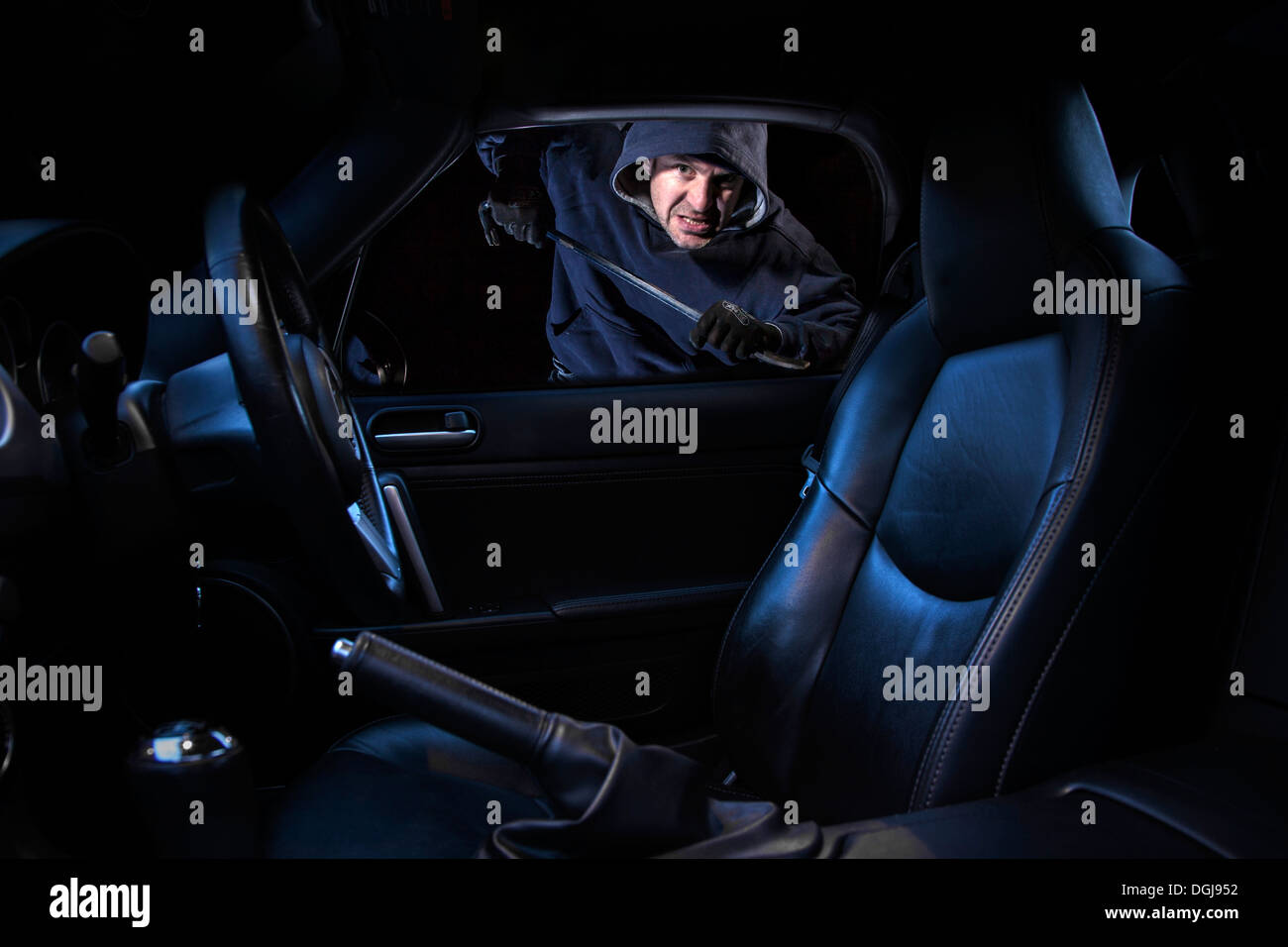 A man breaking into a parked car at night. Stock Photo