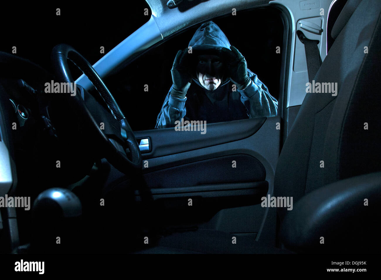 A man looking into a parked car at night. Stock Photo