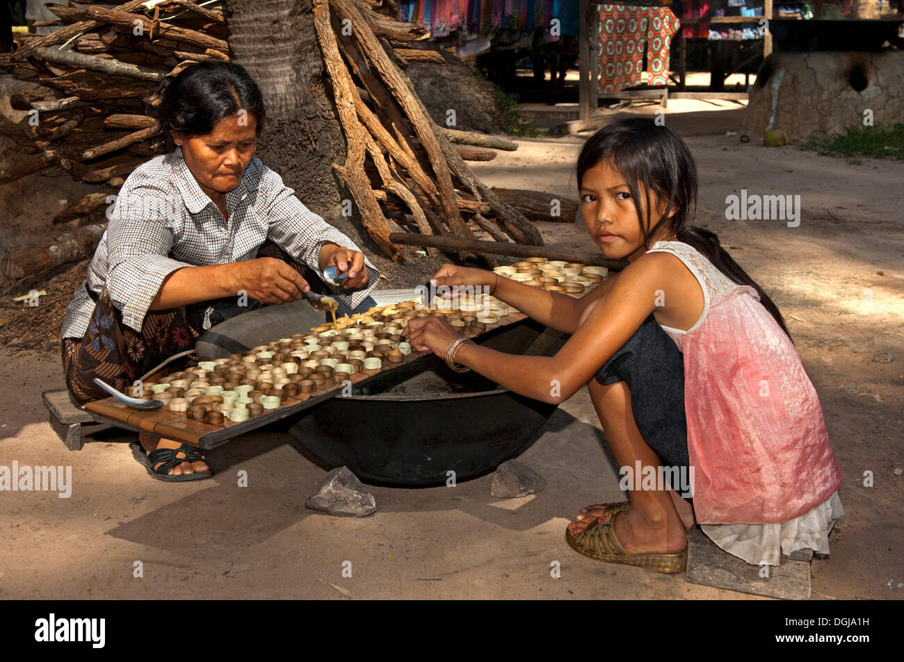 Khmer woman and a girl filling caramelized palm sugar into small moulds made of strips of palm leaves for the production of Stock Photo