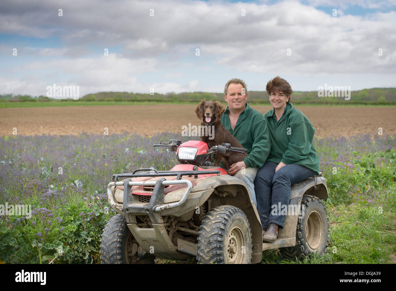 Farmer, wife and pet dog on quad bike in field of organic farm Stock Photo
