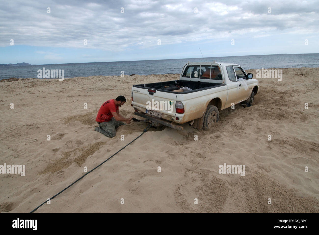 Young man trying to get his trapped pickup car out of the sand Stock Photo