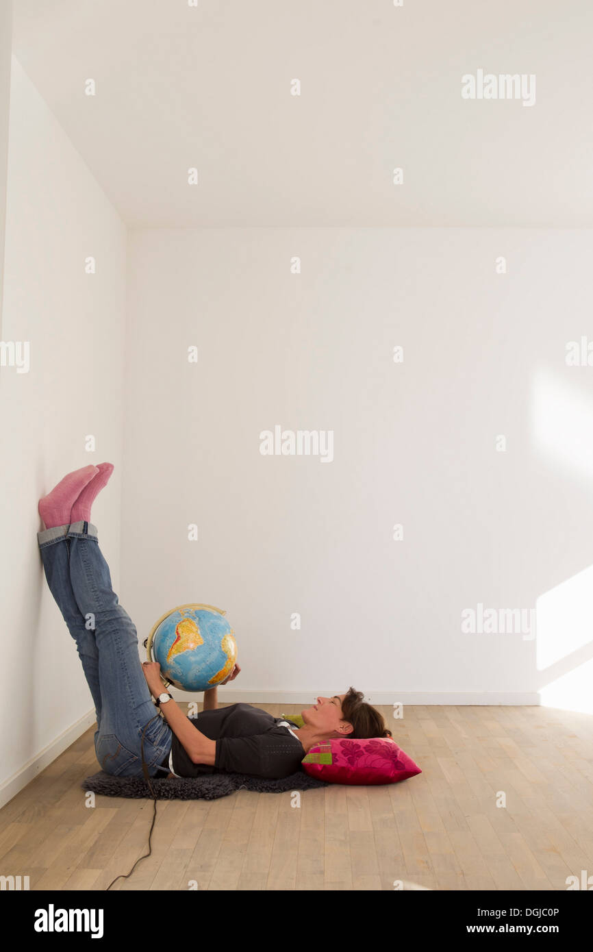 Woman lying on floor of empty room holding globe Stock Photo