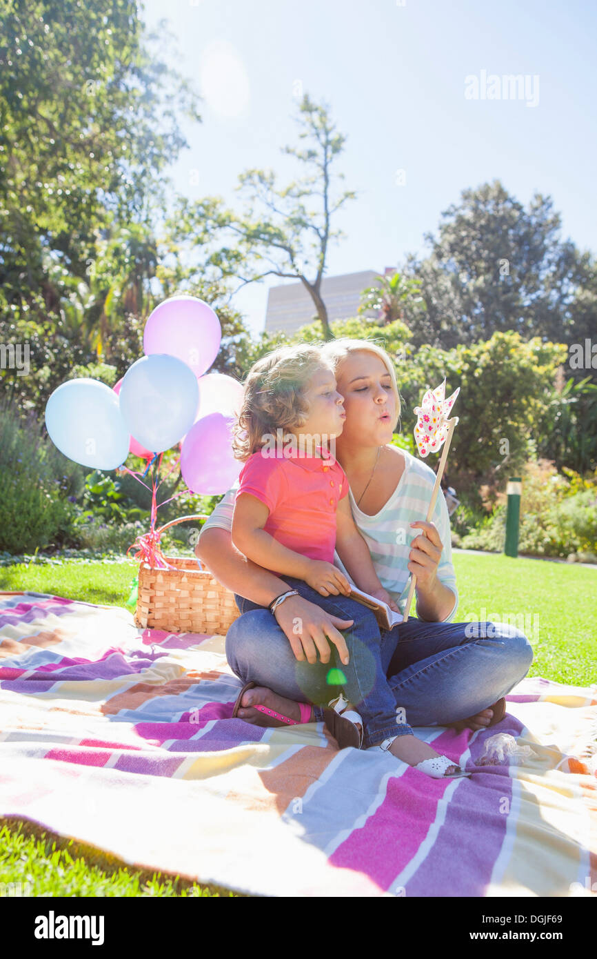 Mother and daughter sitting on blanket in garden with pinwheel Stock