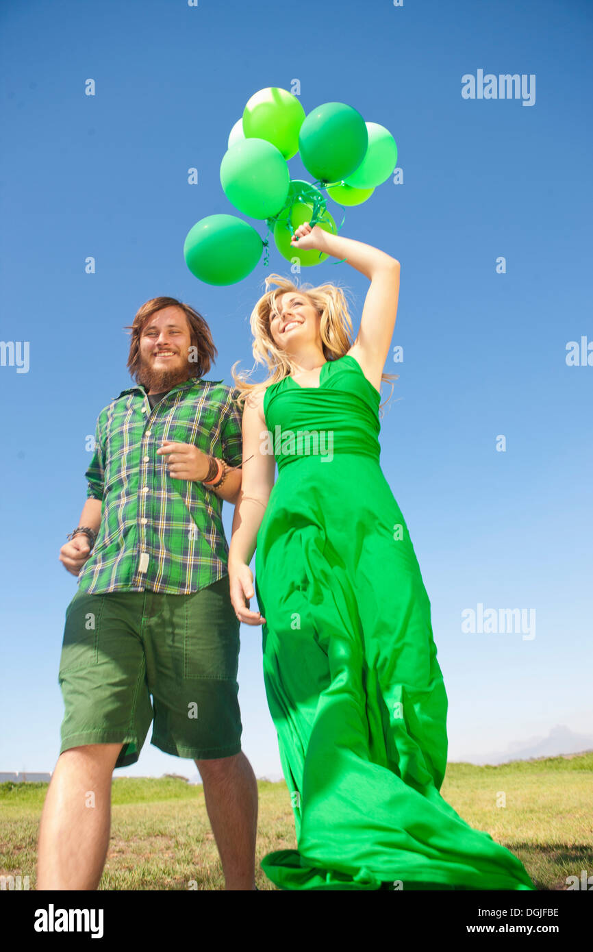 Young couple in field, woman holding green balloons Stock Photo - Alamy