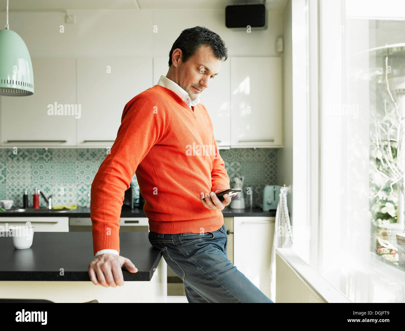 Mature man using cellphone in kitchen Stock Photo