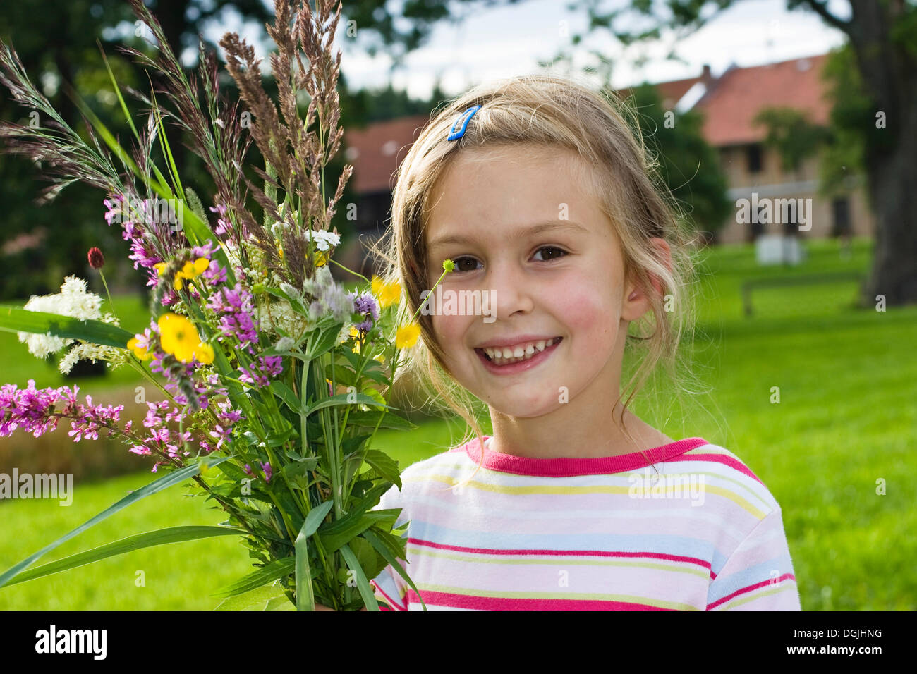 Blond girl, 6, holding a bunch of wild flowers in front of a farmhouse, Bavaria Stock Photo