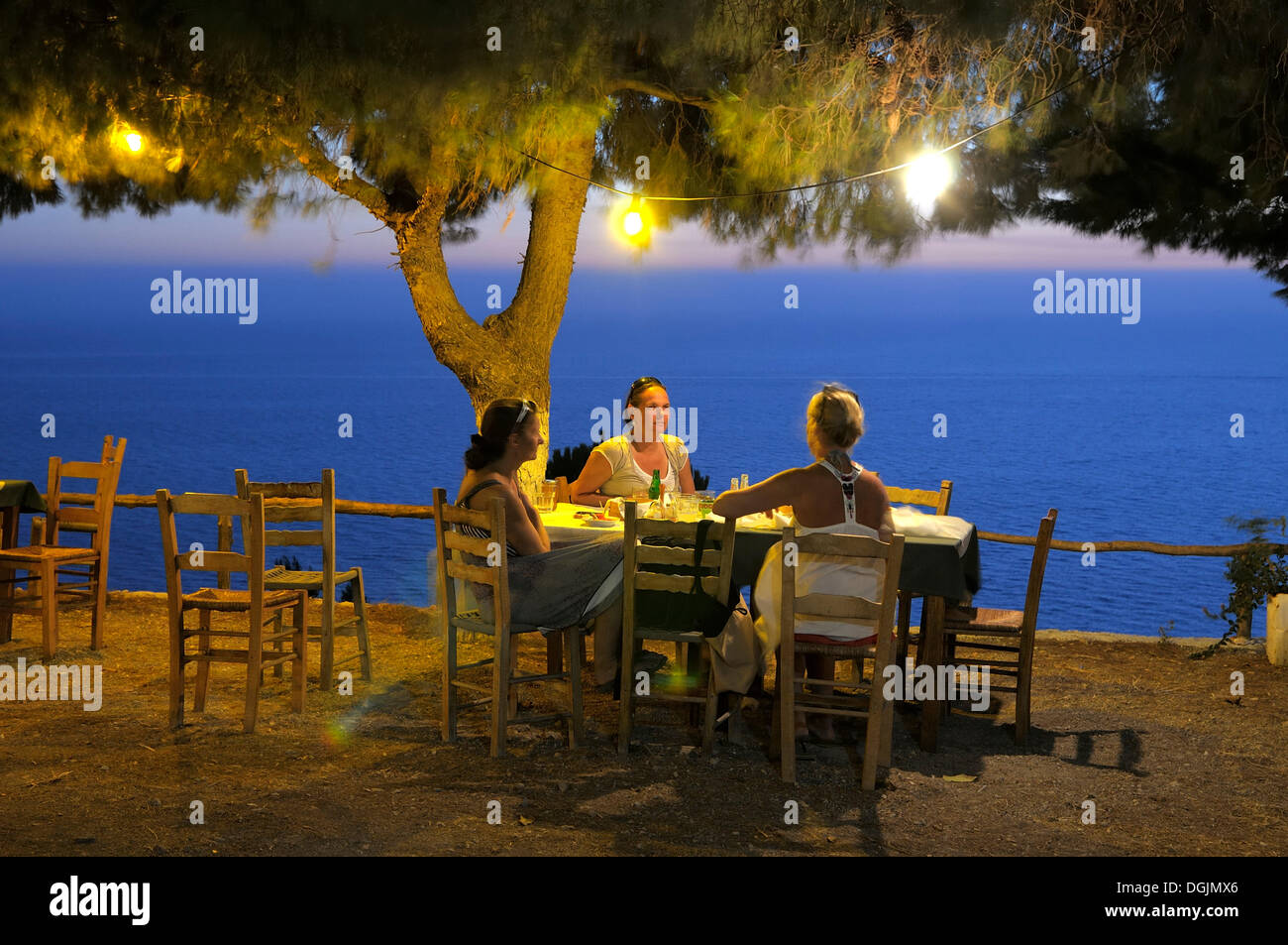 Three women sitting at a table under a tree, in a Greek seaside garden in the evening, Lefkas, Greece, Europe Stock Photo