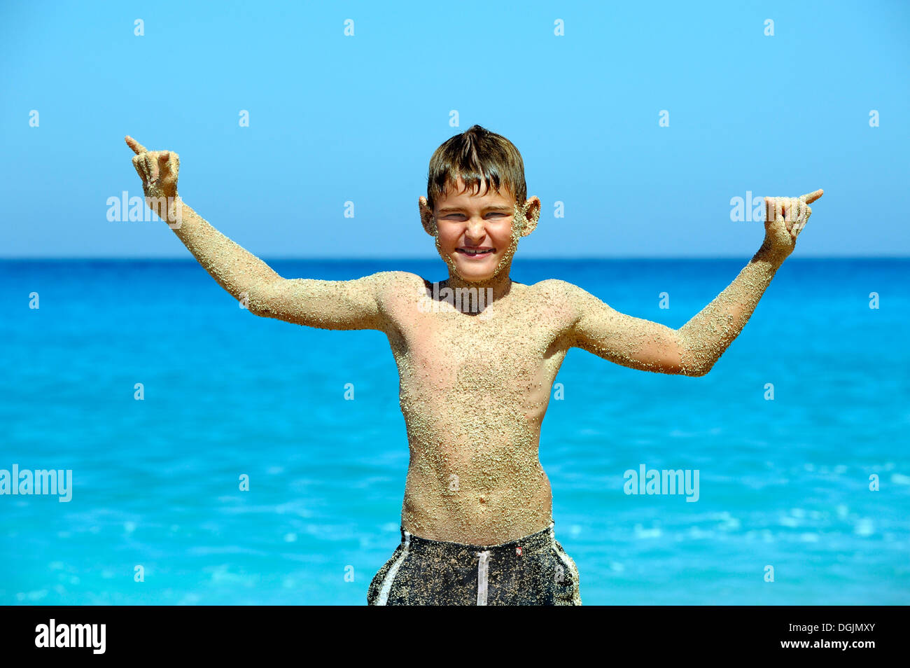 Boy, 9 years, standing on the beach with a sand-covered torso and raising his arms, Kathisma, Lefkas or Lefkada, Greece, Europe Stock Photo