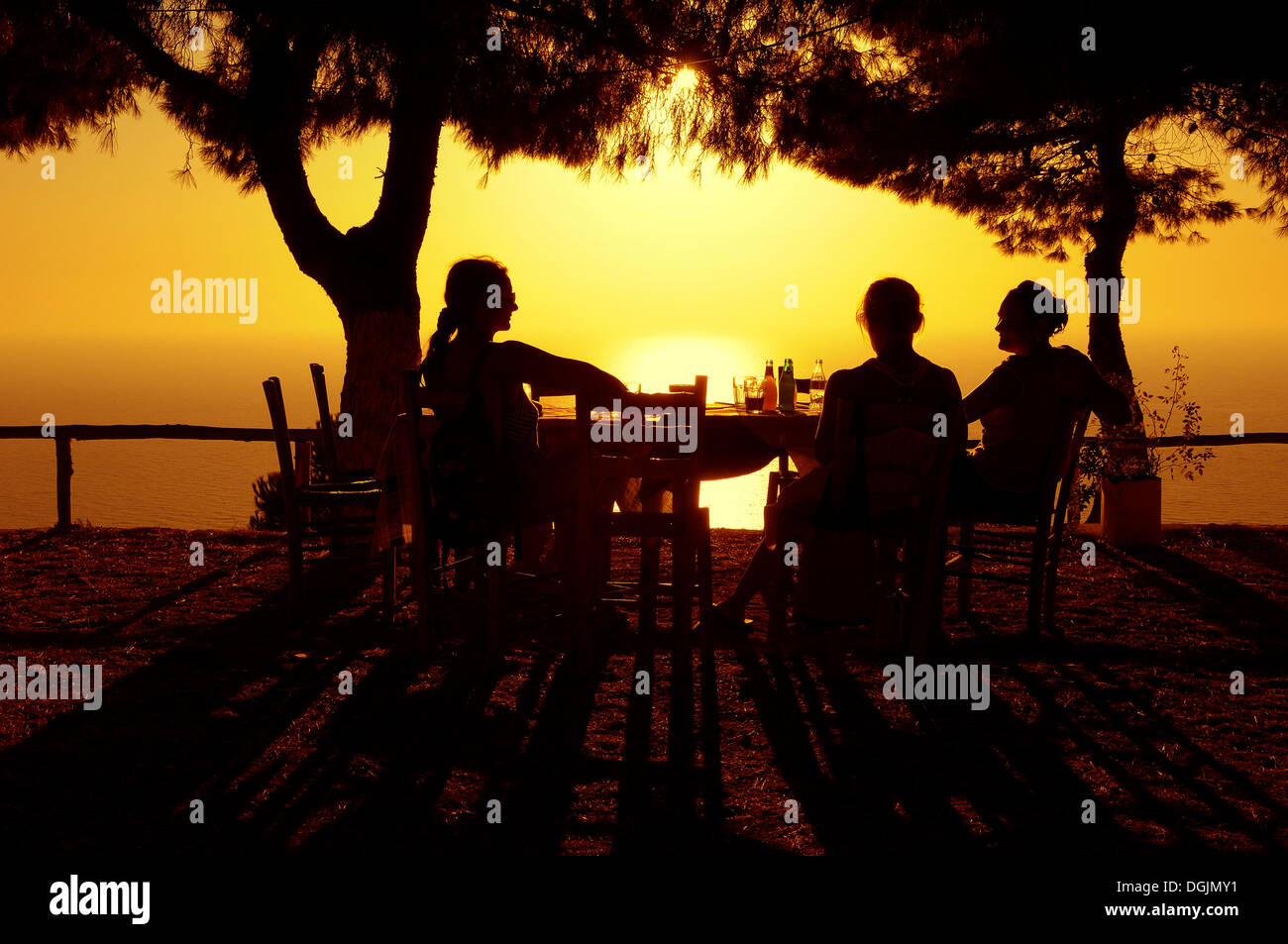 Three women sitting at a table in a seaside garden at sunset, Lefkas, Greece, Europe Stock Photo