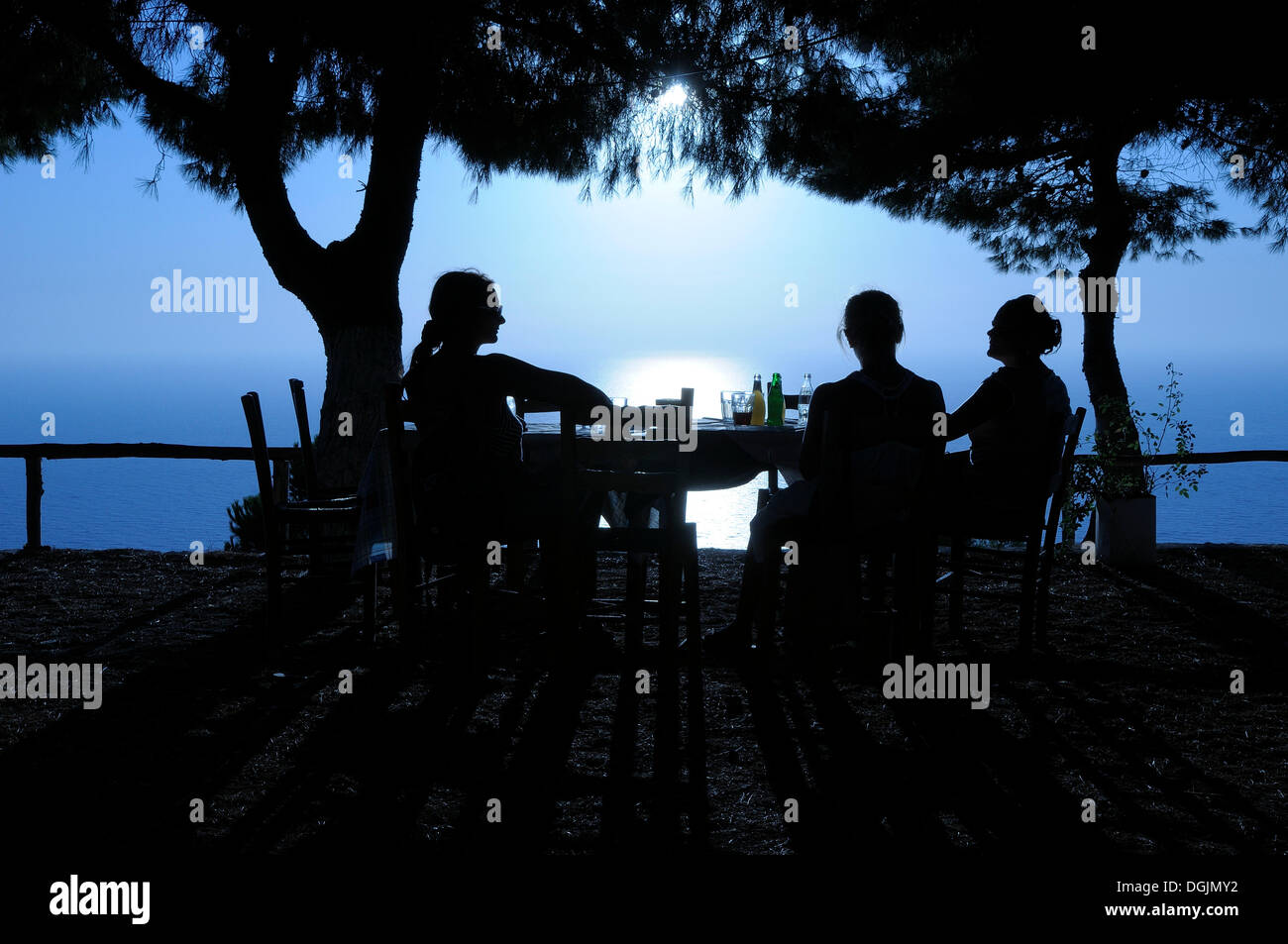Three women sitting at a table in a seaside garden at sunset, Lefkas, Greece, Europe Stock Photo