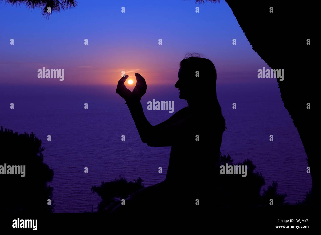 Silhouette of a woman against the sunset sky, her hands enclosing the setting sun, Lefkas, Greece, Europe Stock Photo