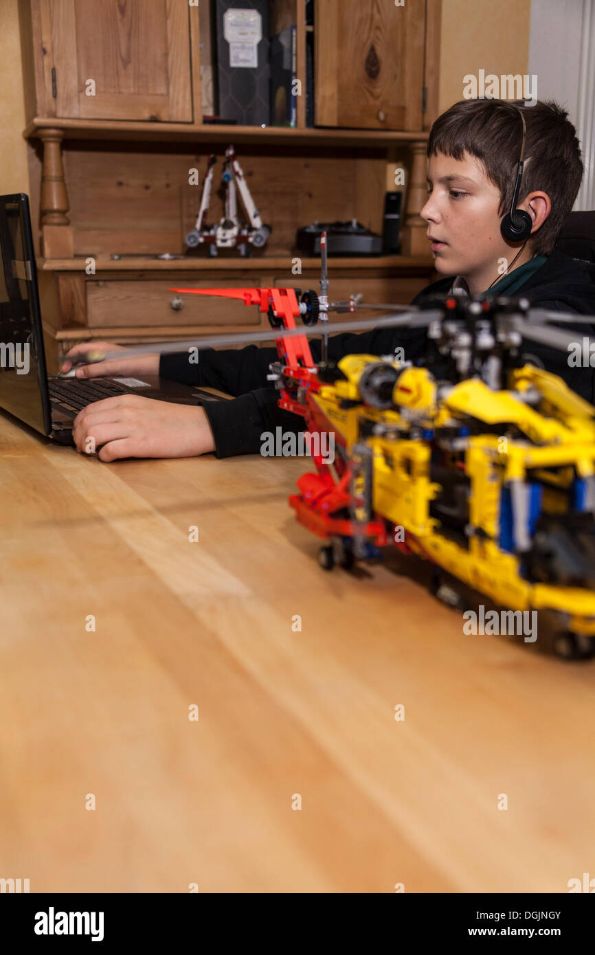 Boy, 12 years, chattingon a laptop with headphones, in front a Lego construction set Stock Photo