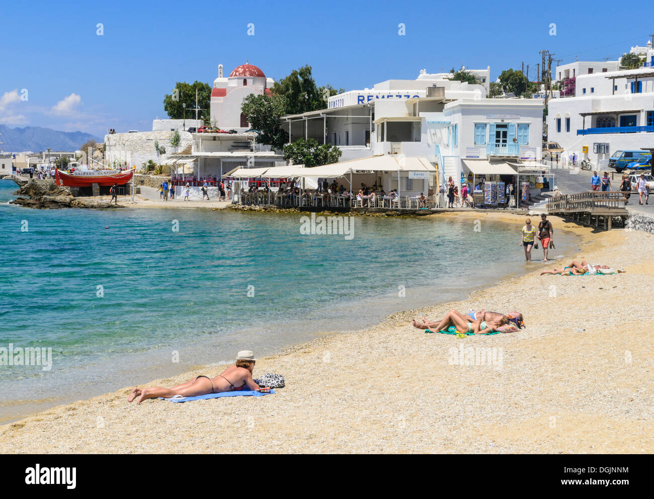 People sunbathing on Mykonos town beach and whitewashed seaside taverna's, Mykonos, Cyclades, Greece Stock Photo