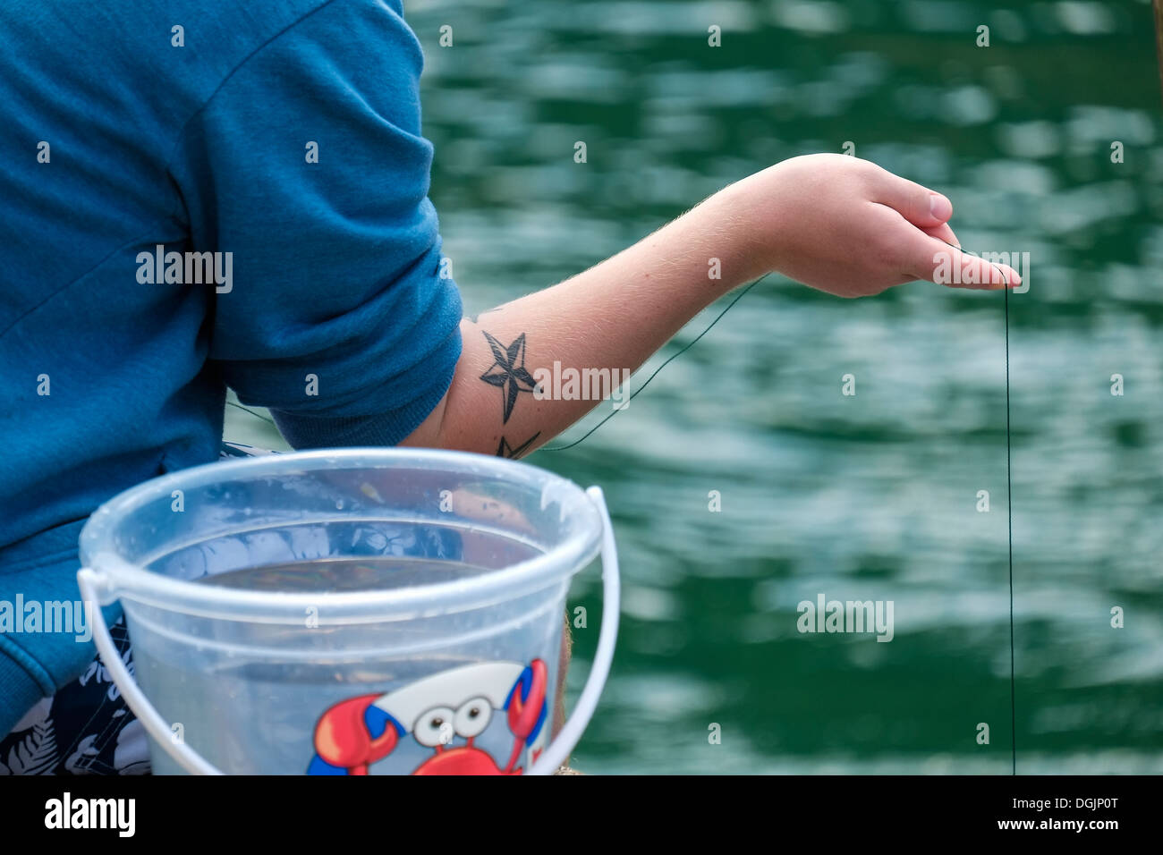 A tattooed person fishing for crabs. Stock Photo