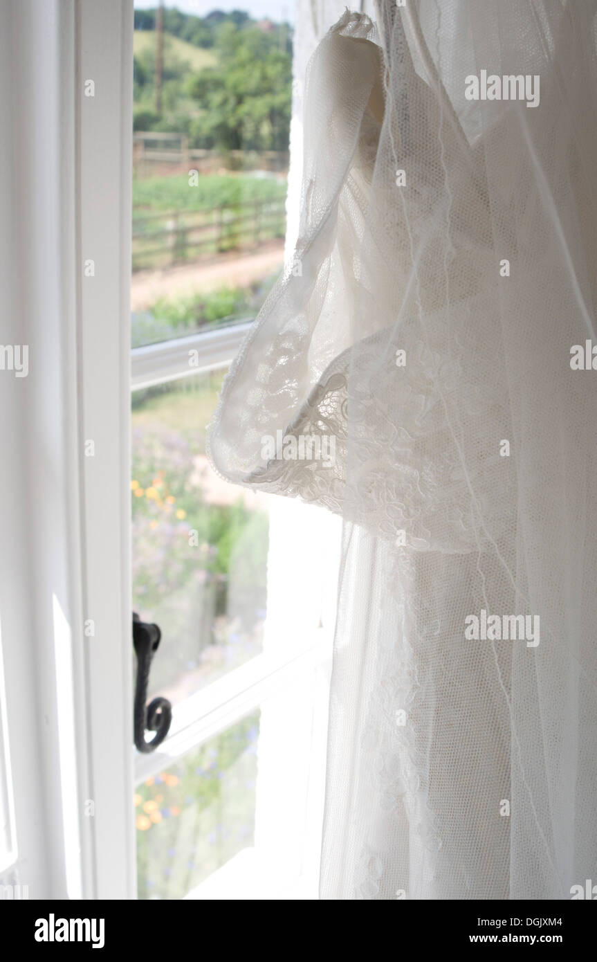 A lace wedding dress by the window, view of an English garden through the window. Stock Photo