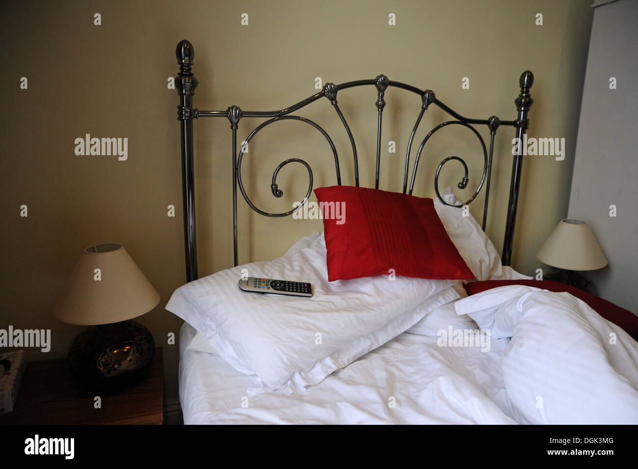 Unmade bed with tv remote control on pillows Stock Photo