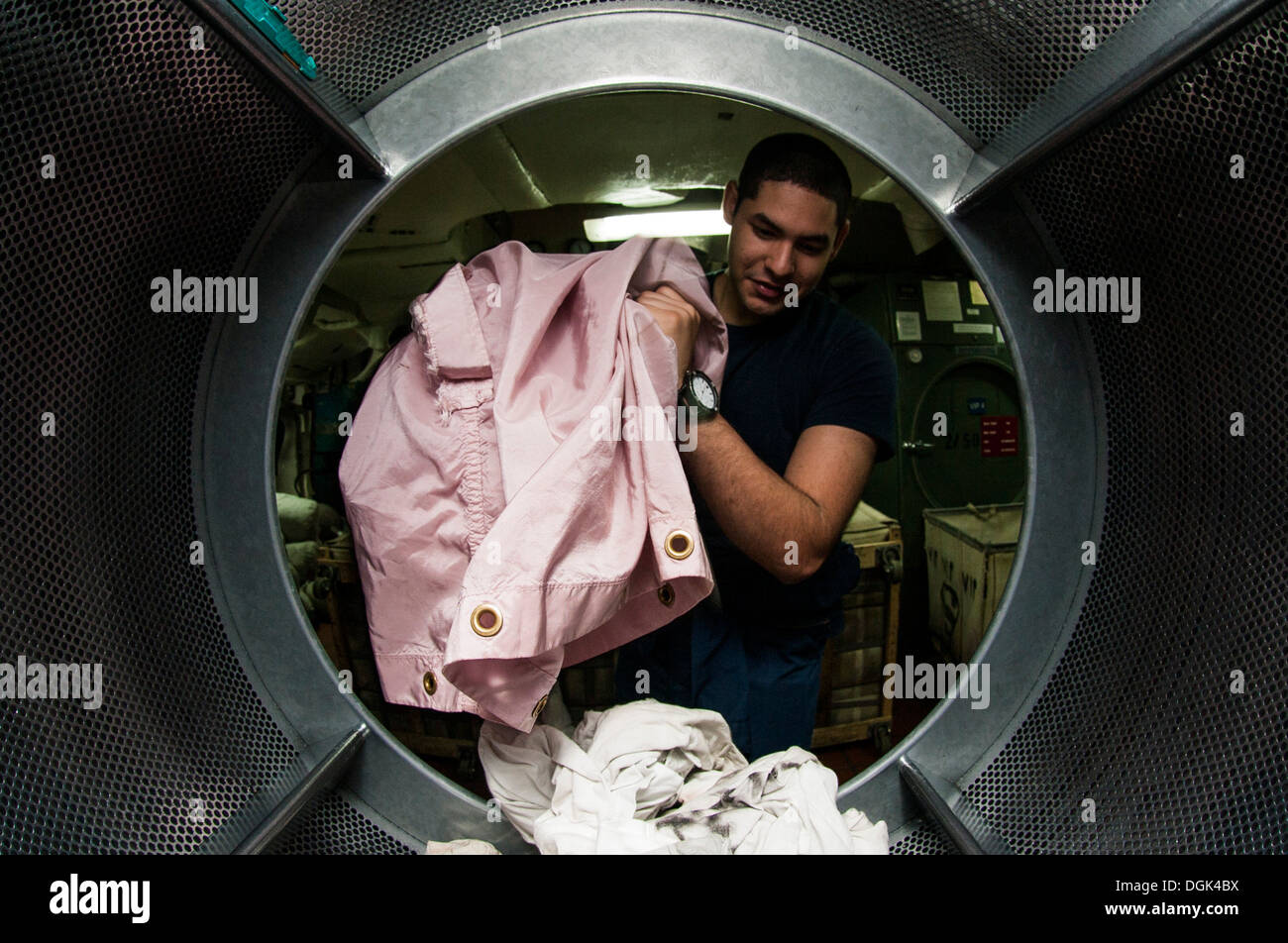 Machinist Mate Fireman Miranda Rivera, from Caglias, Puerto Rico, throws laundry into a dryer aboard the aircraft carrier USS G Stock Photo
