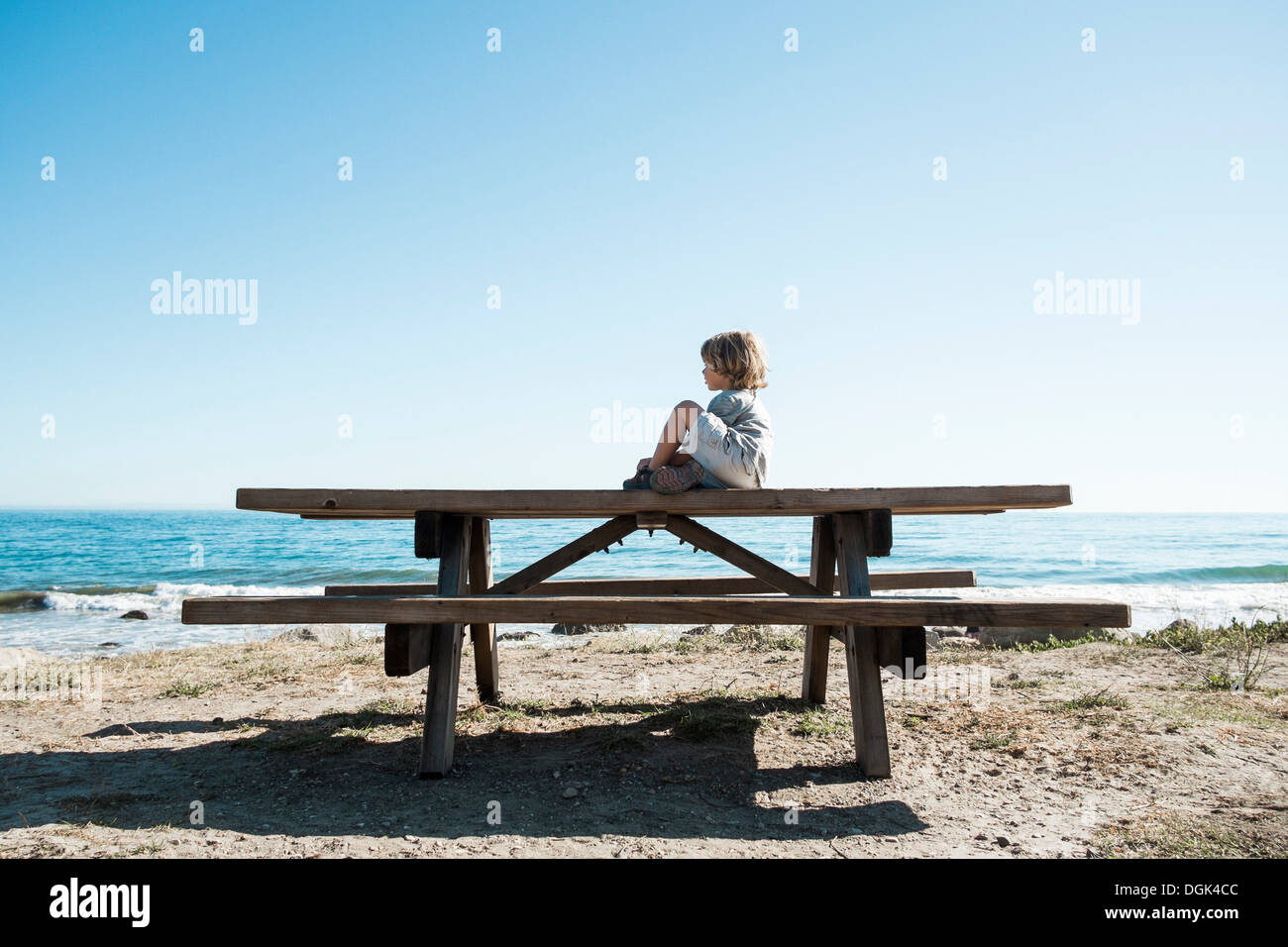 Boy sitting on picnic table at beach Stock Photo