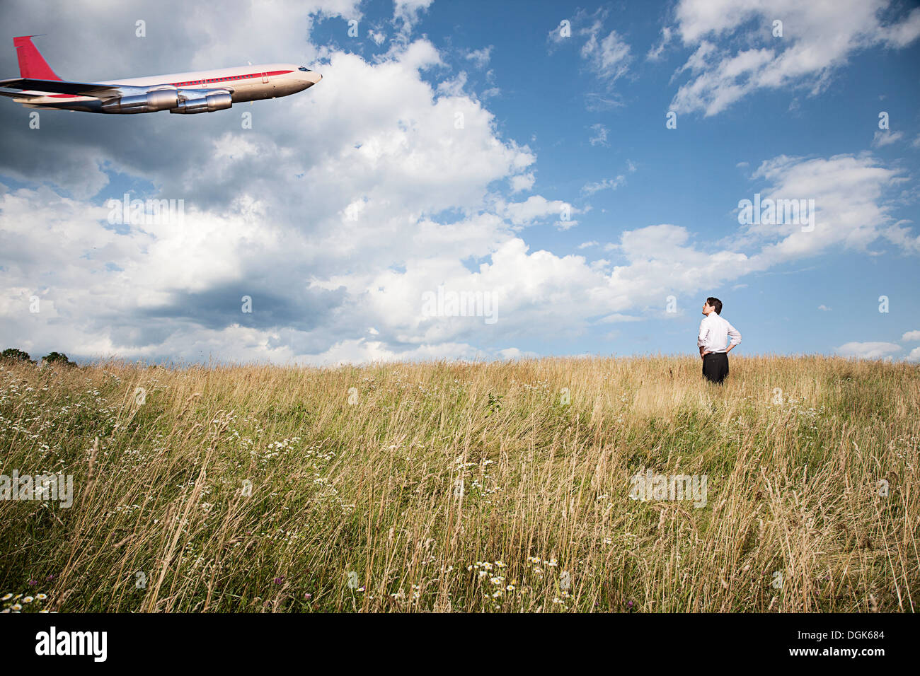 Businessman in field looking at airplane Stock Photo