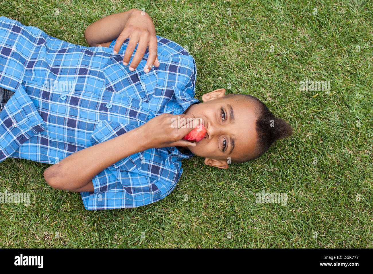 Overhead portrait of boy lying on grass eating plum Stock Photo