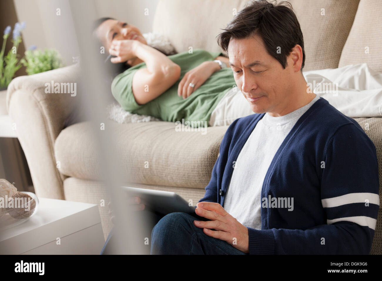 Mature man using digital tablet, woman lying on sofa Stock Photo