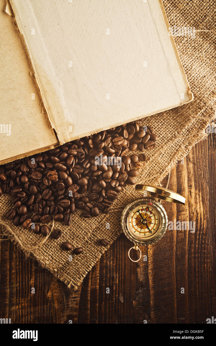 Coffee beans and compass on open book on jute canvas texture. Stock Photo