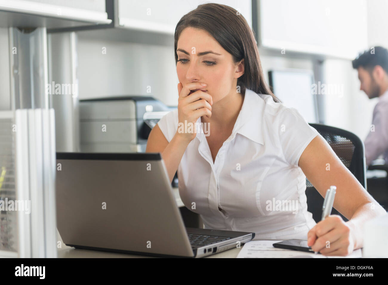 Woman working in office, man in background Stock Photo