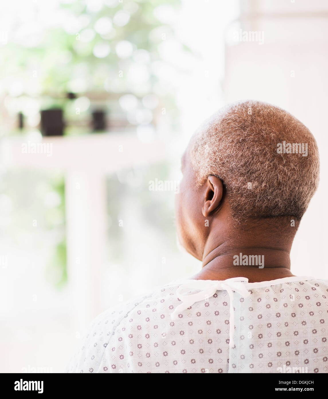 Rear view of patient wearing surgical gown and looking through window Stock Photo